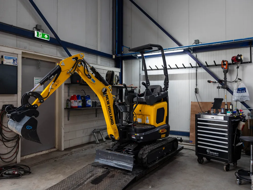 Gele New Holland Construction minigraver in de werkplaats van Voets Hazerswoude